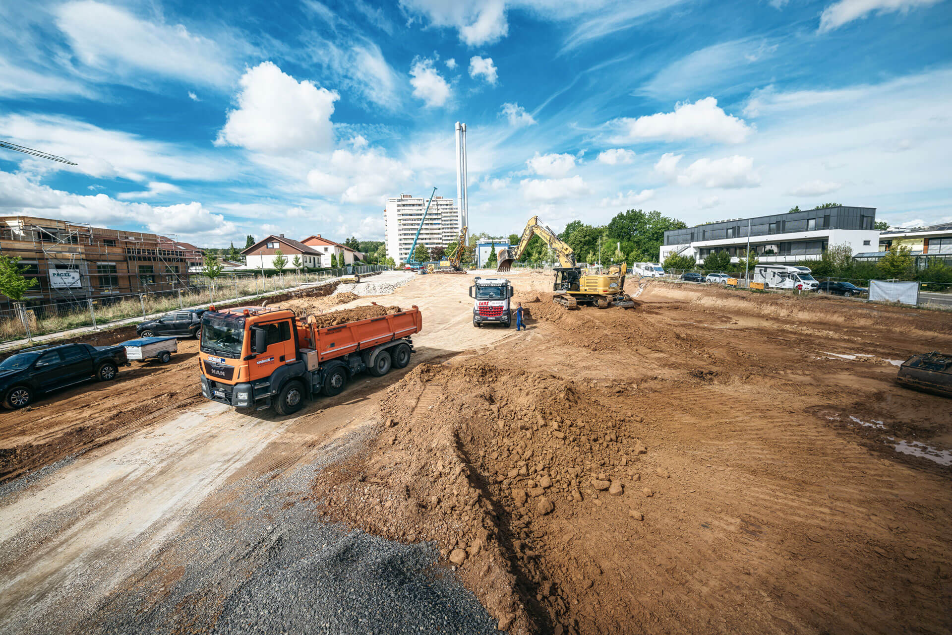 Baustellenansicht mit Baggern und Lastwagen, die Erde abtransportieren.