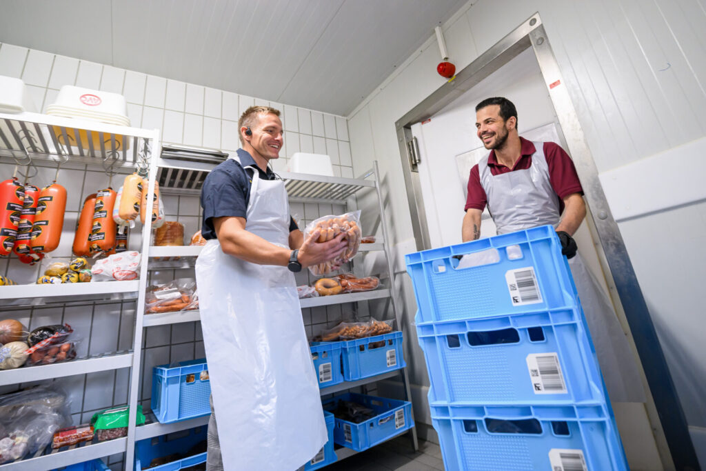 Ronald Petermann und George holen Fleisch und Würste aus dem Kühlraum der Edeka-Fleischabteilung.