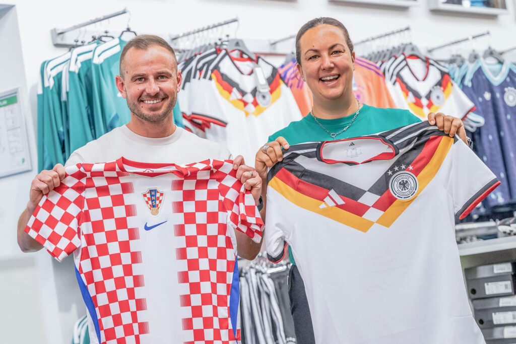 Melanie und Zoran halten das deutsche und das kroatische Weltmeisterschaft-Trikot 2026 in die Kamera.