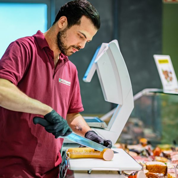 Syrer George schneidet an der Wursttheke eine Fleischwurst in Stücke.