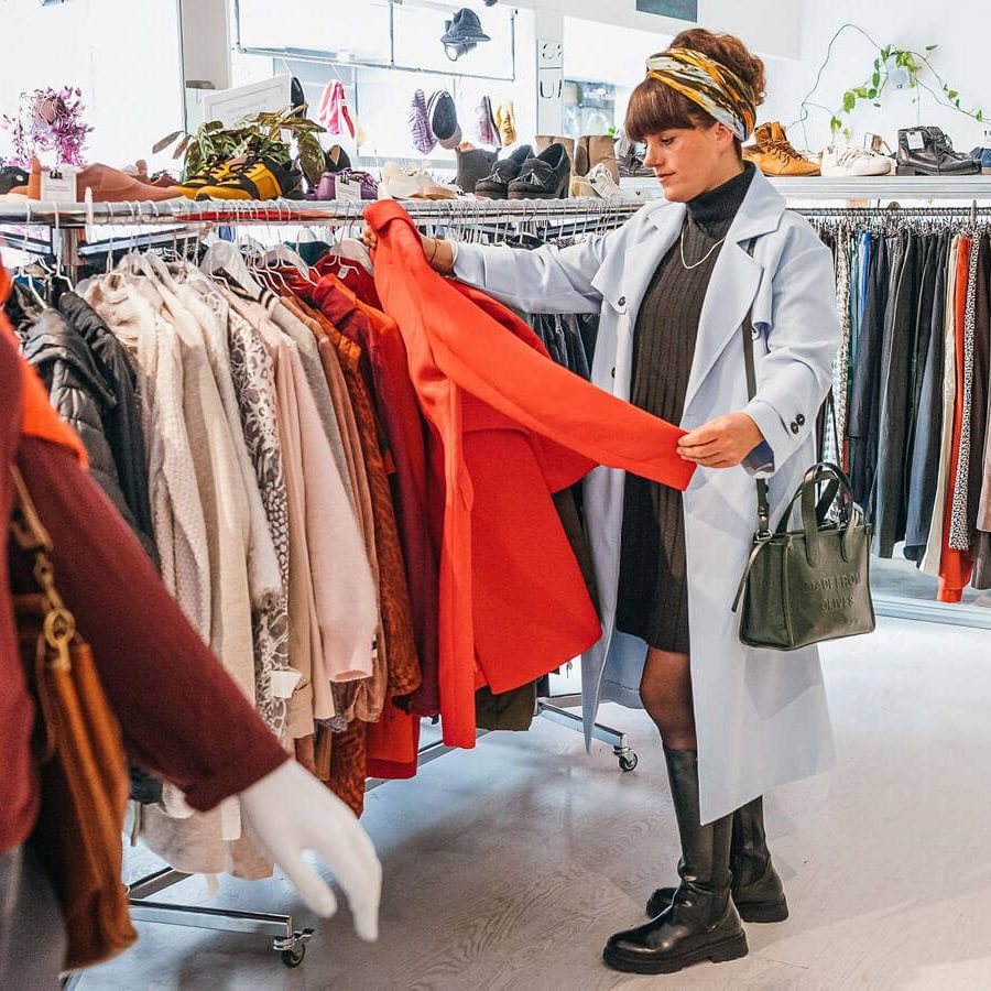 Kostümbildnerin Tini begutachtet einen roten Mantel vor einer Kleiderstange.